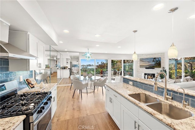 kitchen with hanging light fixtures, a sink, a fireplace, light wood-style floors, and stainless steel gas stove