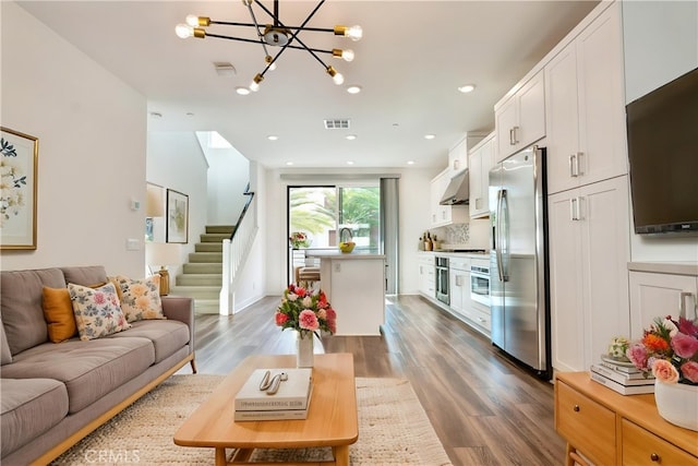living room with an inviting chandelier, stairs, wood finished floors, and visible vents