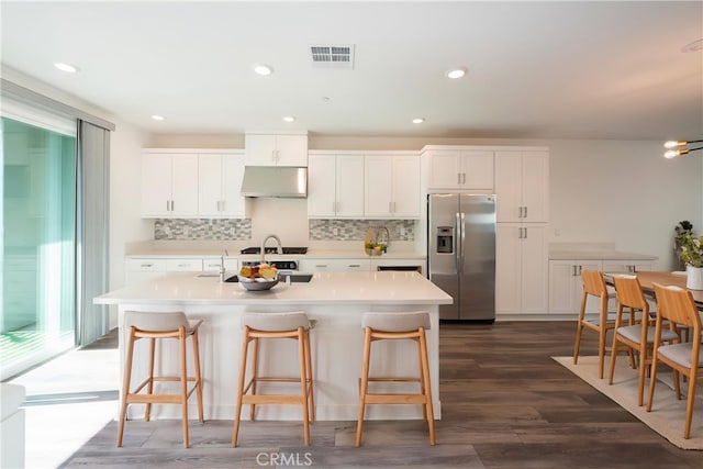 kitchen featuring stainless steel fridge, backsplash, under cabinet range hood, and visible vents