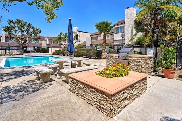 pool featuring a residential view, a patio area, fence, an outdoor kitchen, and a grill