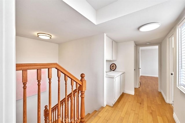 corridor with light wood-style floors, baseboards, and an upstairs landing