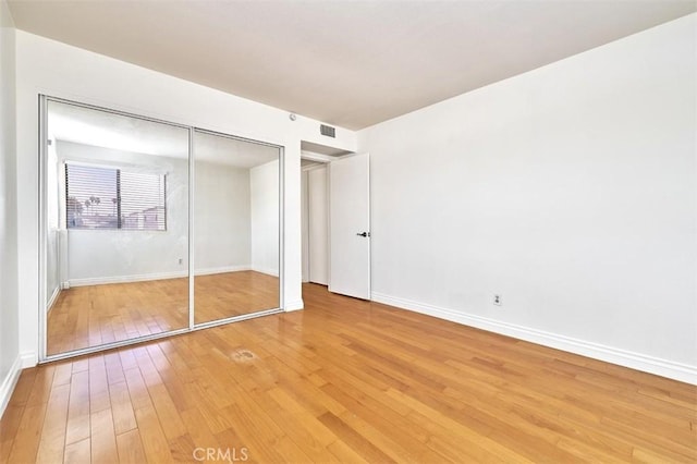 unfurnished bedroom with a closet, baseboards, visible vents, and light wood-type flooring