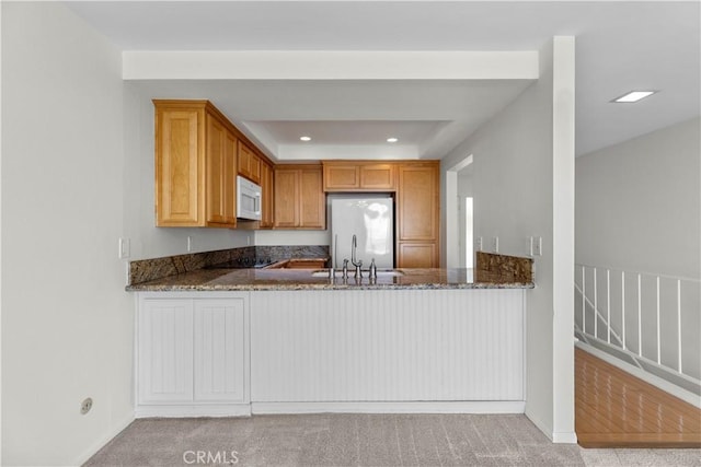kitchen with stainless steel refrigerator, white microwave, dark stone counters, a sink, and carpet