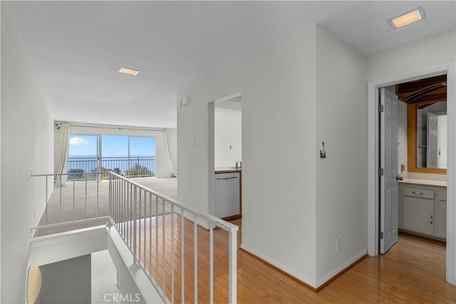 hall with light wood-type flooring, baseboards, a water view, and an upstairs landing