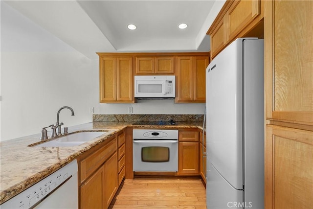 kitchen with white appliances, light stone countertops, light wood-type flooring, recessed lighting, and a sink