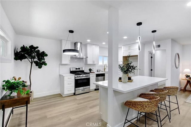 kitchen with wall chimney range hood, light wood-type flooring, light countertops, white cabinets, and appliances with stainless steel finishes
