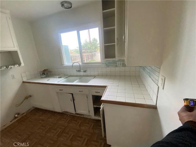 kitchen featuring a sink, open shelves, tile counters, white cabinetry, and decorative backsplash