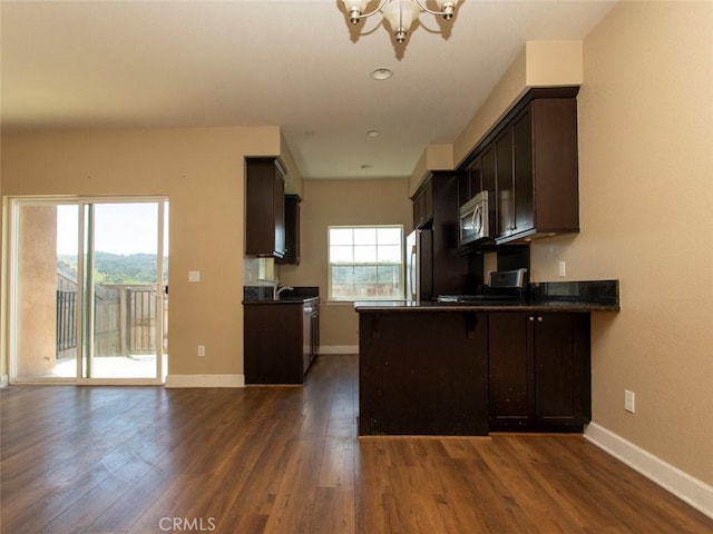 kitchen featuring dark countertops, a chandelier, stainless steel microwave, refrigerator, and dark wood-style floors