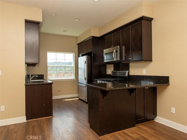 kitchen featuring dark brown cabinetry, dark wood finished floors, baseboards, a breakfast bar, and stainless steel appliances