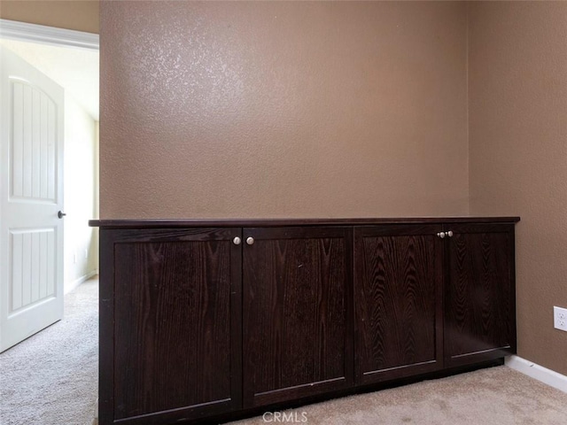 interior space with baseboards, a textured wall, and light carpet