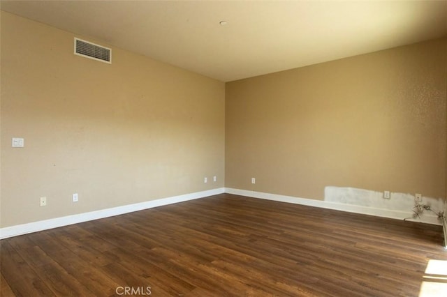 unfurnished room featuring visible vents, dark wood-style flooring, and baseboards