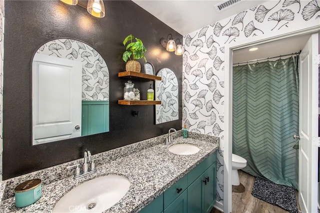 bathroom featuring a sink, toilet, double vanity, and wood finished floors
