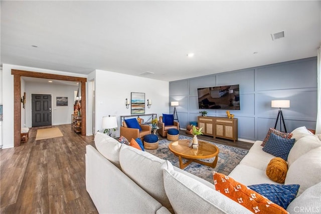 living area featuring visible vents, wood finished floors, baseboards, a decorative wall, and recessed lighting