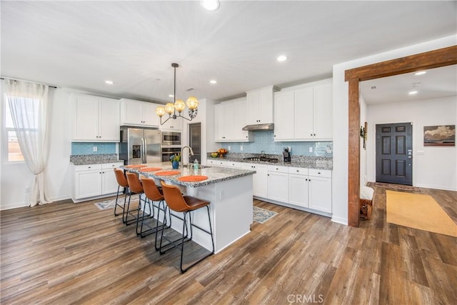 kitchen with decorative backsplash, appliances with stainless steel finishes, dark wood finished floors, an inviting chandelier, and a breakfast bar