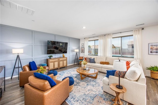 living room featuring baseboards, a decorative wall, wood finished floors, and visible vents