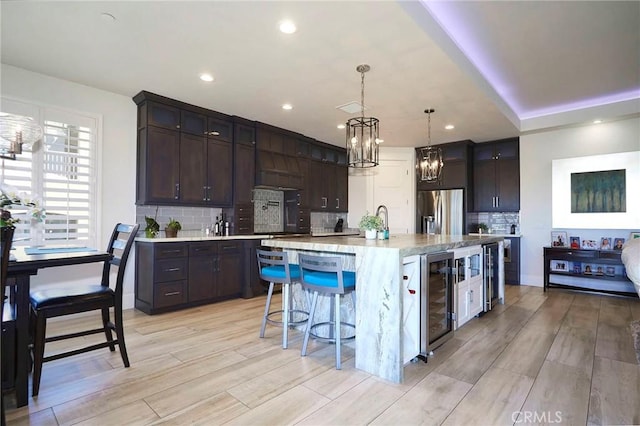 kitchen featuring dark brown cabinetry, a kitchen breakfast bar, stainless steel refrigerator with ice dispenser, a chandelier, and tasteful backsplash