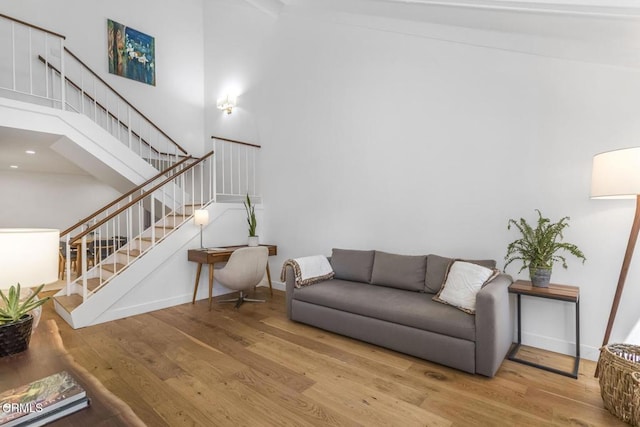 living area with stairs, a high ceiling, baseboards, and wood finished floors