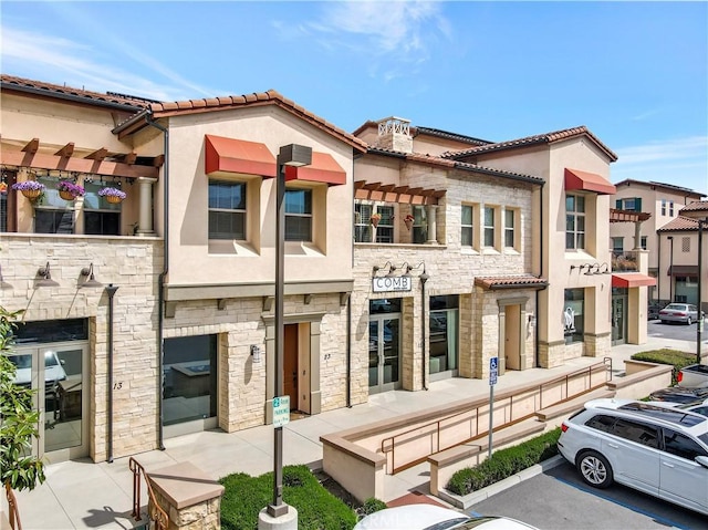 view of front facade featuring a tiled roof, uncovered parking, stone siding, and stucco siding