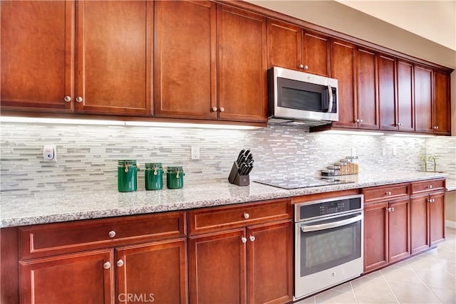 kitchen featuring dark brown cabinets, light stone countertops, tasteful backsplash, appliances with stainless steel finishes, and light tile patterned floors