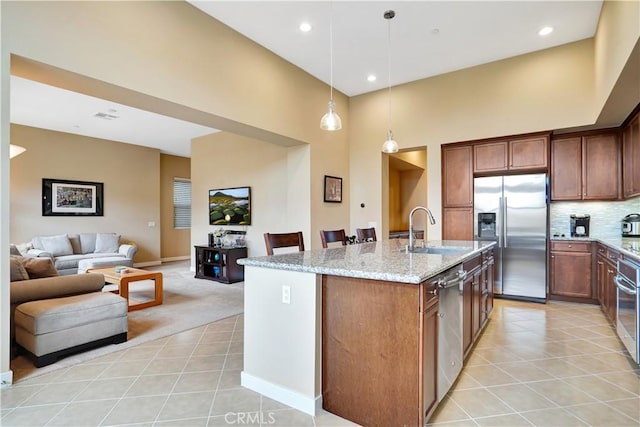 kitchen with light stone countertops, a sink, open floor plan, a high ceiling, and stainless steel appliances