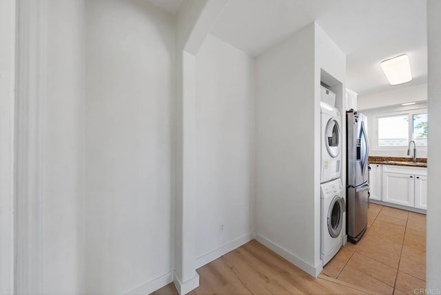 laundry area with baseboards, stacked washer and dryer, laundry area, and a sink