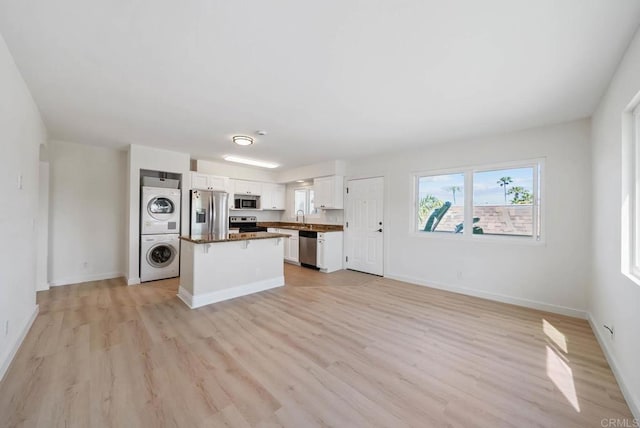 kitchen with a kitchen island, appliances with stainless steel finishes, white cabinetry, stacked washing maching and dryer, and light wood-style flooring