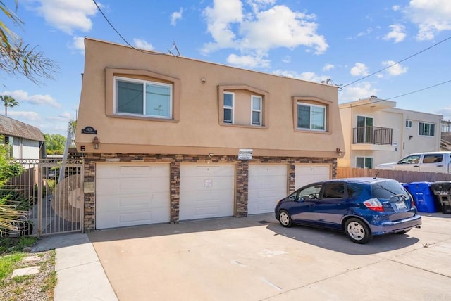 multi unit property featuring fence, an attached garage, stone siding, stucco siding, and concrete driveway