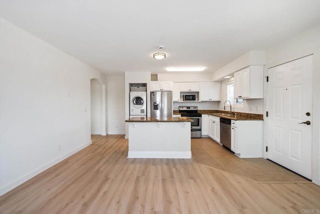 kitchen with stacked washer and clothes dryer, arched walkways, white cabinets, a sink, and appliances with stainless steel finishes