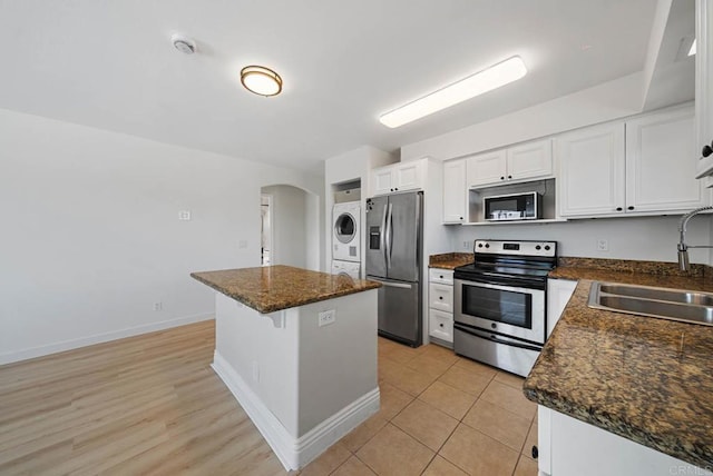 kitchen featuring stacked washer and clothes dryer, a center island, arched walkways, a sink, and appliances with stainless steel finishes