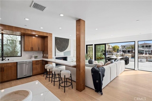 kitchen with visible vents, brown cabinetry, light countertops, light wood finished floors, and dishwasher