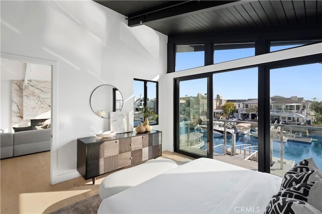 bedroom featuring access to outside, beamed ceiling, wood finished floors, and a towering ceiling