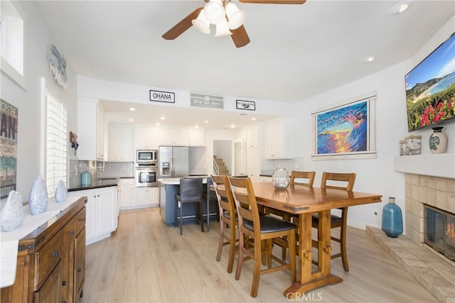 dining space featuring light wood-style floors, a ceiling fan, recessed lighting, and a fireplace