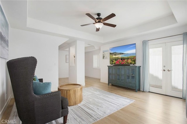 sitting room with a ceiling fan, a tray ceiling, and wood finished floors