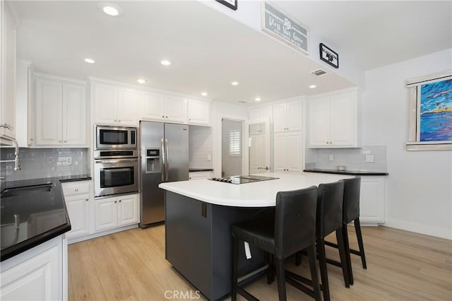 kitchen with a sink, appliances with stainless steel finishes, tasteful backsplash, and light wood finished floors