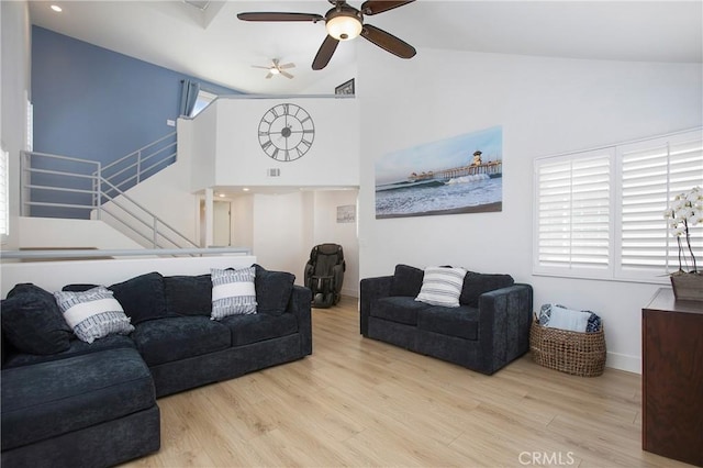 living area with ceiling fan, high vaulted ceiling, baseboards, light wood-type flooring, and stairway