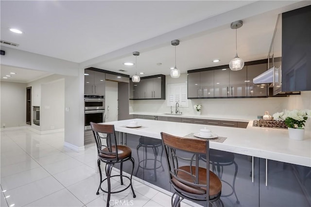 kitchen featuring visible vents, a peninsula, a kitchen breakfast bar, stainless steel double oven, and a sink