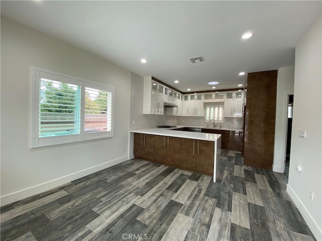 kitchen featuring visible vents, light countertops, white cabinets, a peninsula, and glass insert cabinets