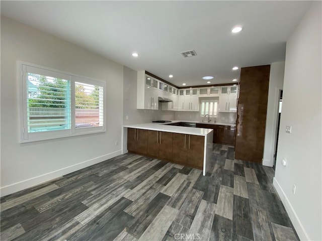 kitchen with a sink, light countertops, a peninsula, visible vents, and glass insert cabinets