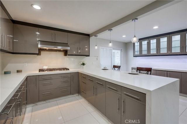 kitchen with a peninsula, under cabinet range hood, gray cabinetry, and stainless steel gas stovetop
