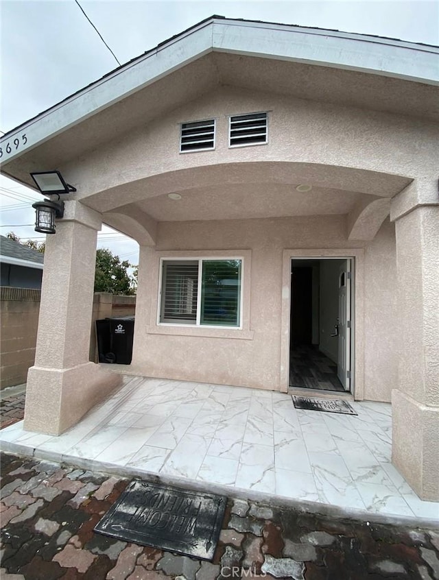 property entrance with fence, a patio area, and stucco siding