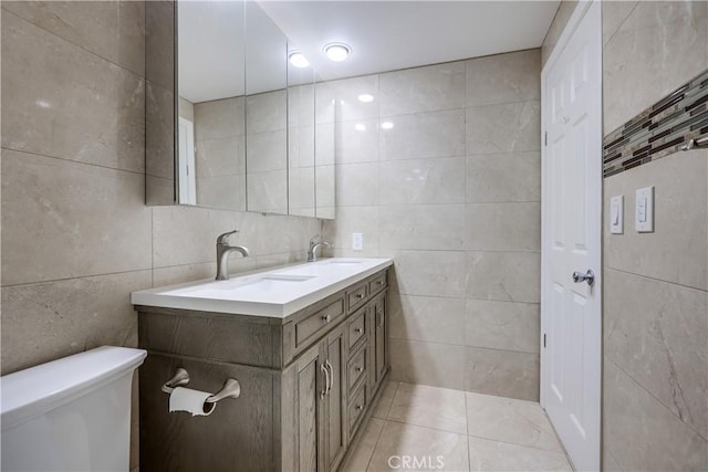 bathroom featuring double vanity, toilet, tile walls, and a sink