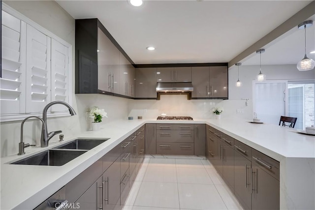 kitchen featuring a peninsula, under cabinet range hood, a sink, light tile patterned floors, and gray cabinetry