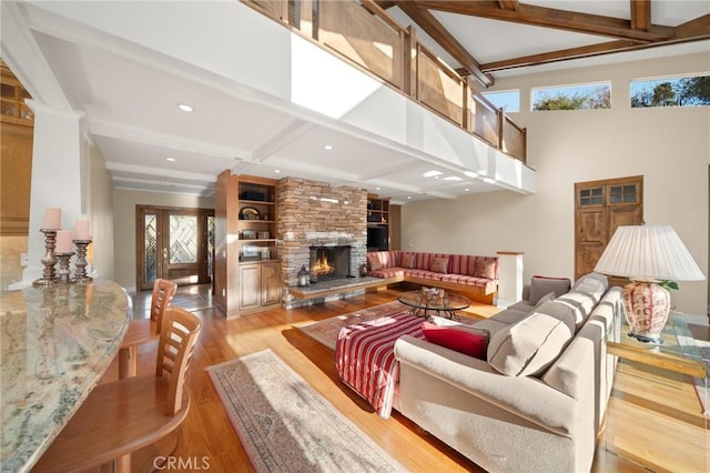 living room with light wood-style floors, beamed ceiling, a stone fireplace, and a healthy amount of sunlight