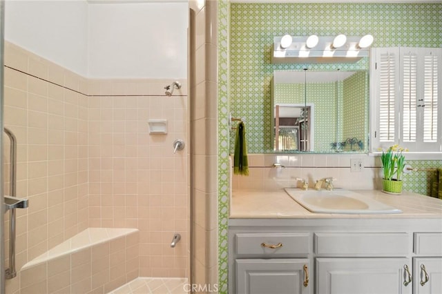 bathroom featuring vanity, a tile shower, and wallpapered walls