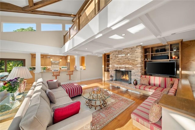 living area with baseboards, beamed ceiling, light wood-type flooring, and a stone fireplace