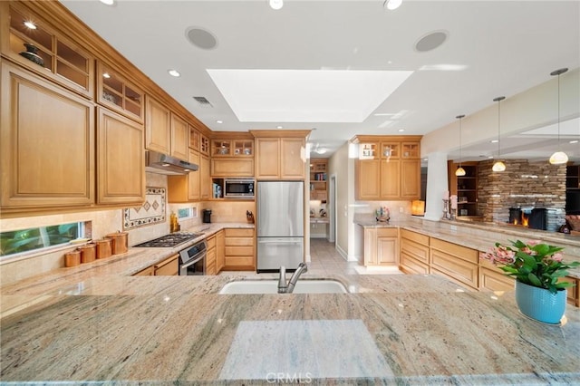 kitchen with light stone countertops, appliances with stainless steel finishes, a sink, a peninsula, and under cabinet range hood