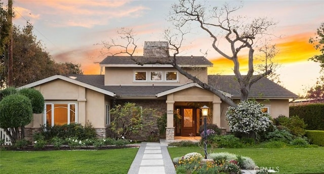 view of front of home with a chimney, stucco siding, a yard, and stone siding