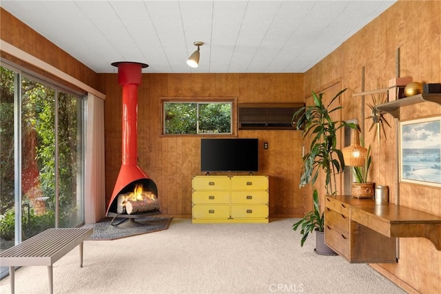 sitting room with plenty of natural light, a wood stove, carpet, and wood walls