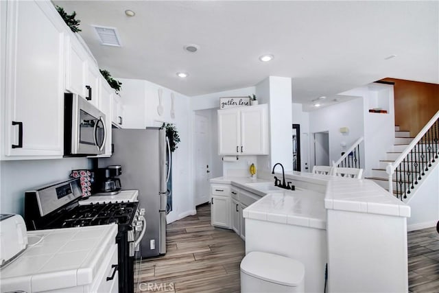 kitchen with tile countertops, a sink, appliances with stainless steel finishes, and a peninsula