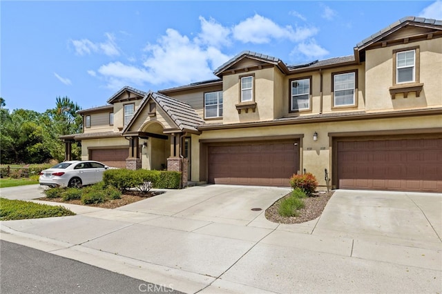 multi unit property with a tiled roof, an attached garage, driveway, and stucco siding